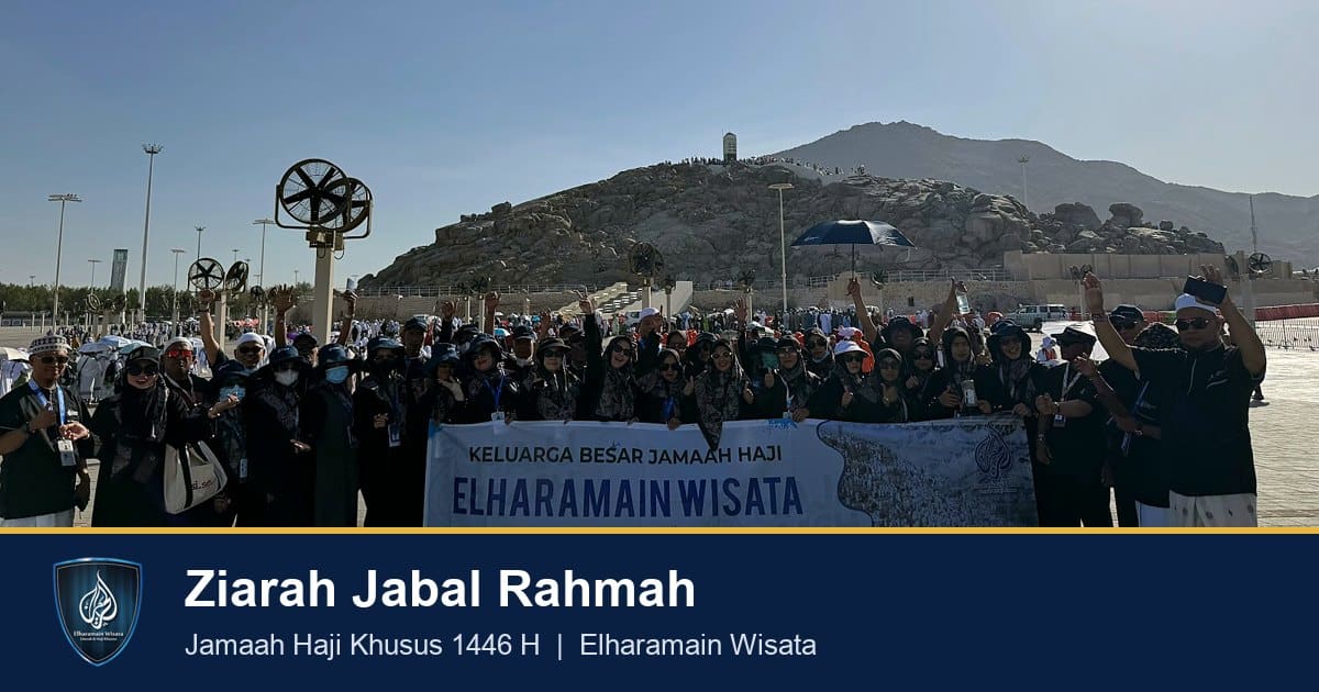 Rombongan jamaah haji Elharamain Wisata membentangkan spanduk saat ziarah jabal rahmah dengan bukit dan tugu putih di belakang